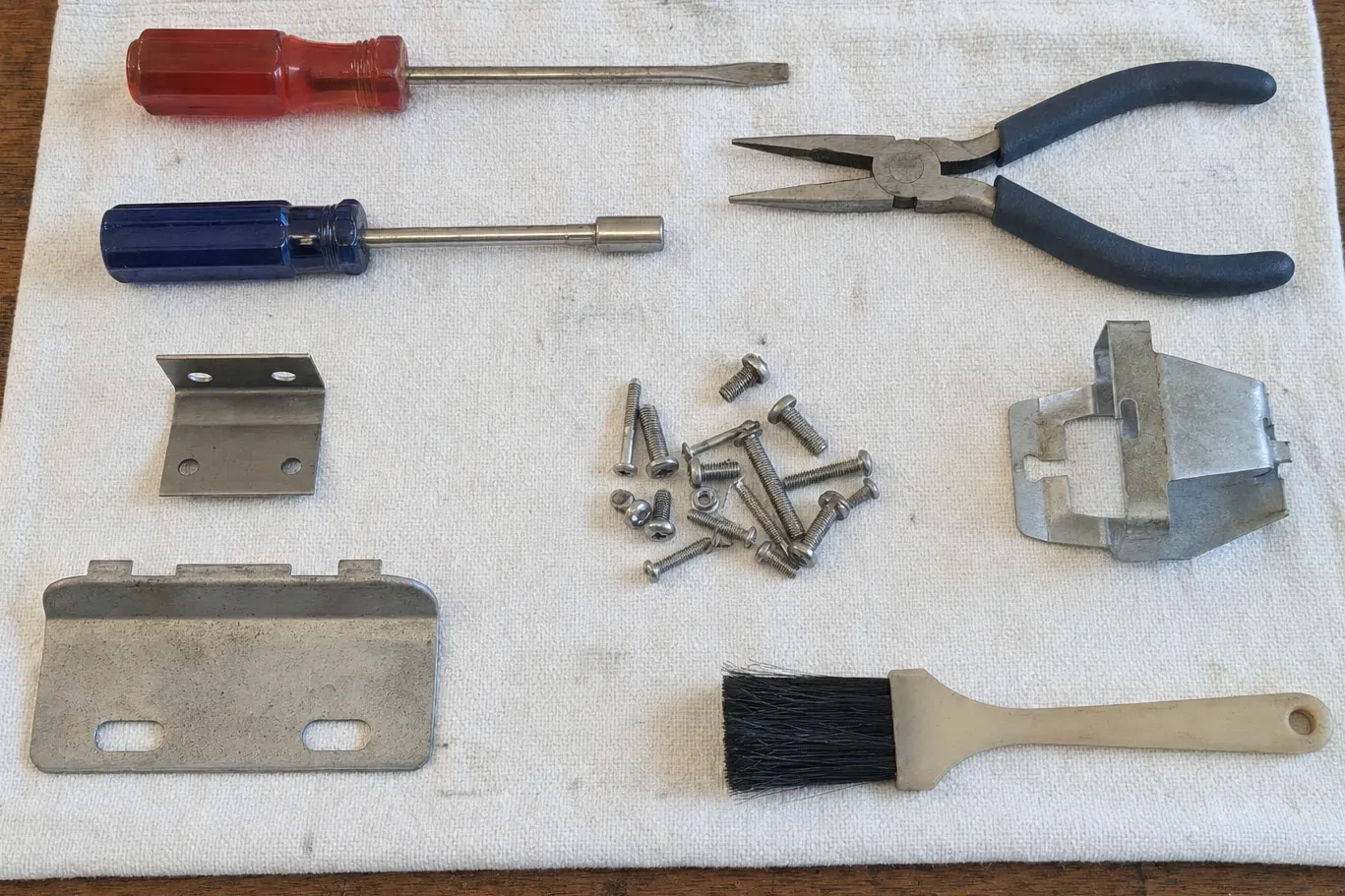 Screwdrivers, needle-nose pliers, a soft brush and galvanised sheet-metal parts laid out on a white cloth