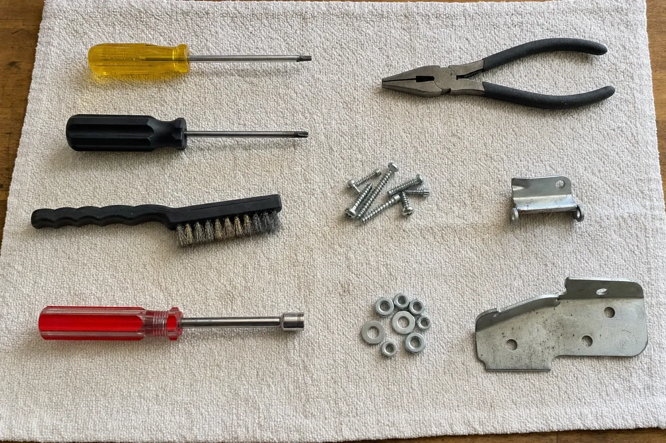 Phillips drivers, a wire brush, combination pliers, sheet-metal screws, washers and two brackets on a towel